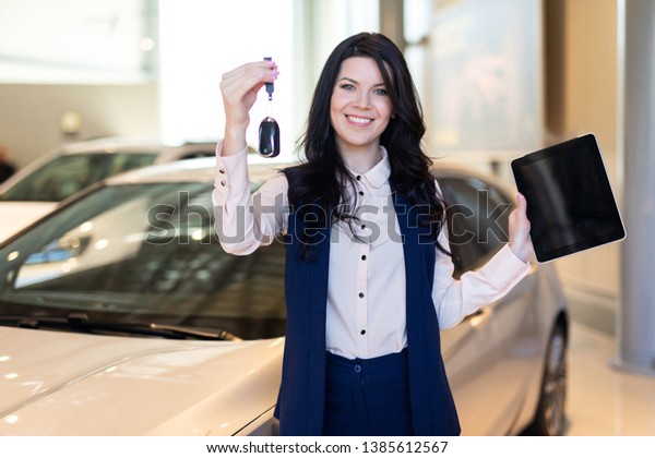 Happy woman buyer possing with keys near her
new vehicle in car
dealership