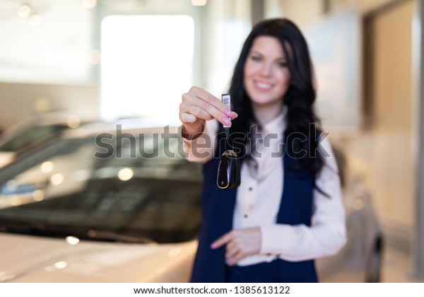 Happy woman buyer possing with keys near her
new vehicle in car
dealership