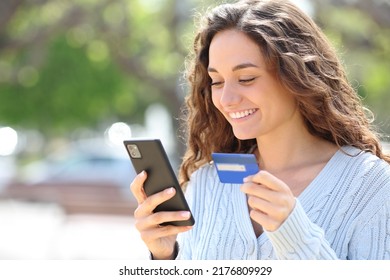 Happy woman buying online with credit card and cell phone in the street