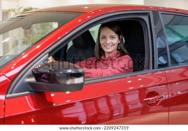 happy woman buys a red car at a car dealership.\
signing a trade-in contract and handing over keys, shaking hands. A\
successful woman chooses a new car. Rent a vehicle or repair\
service center.