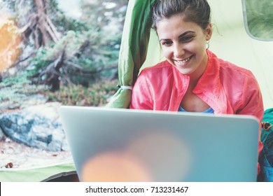 Happy Woman Camping In The Wilderness Inside Her Cozy Little Tent. Working On Laptop In The Journey