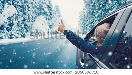 Happy woman in the car gesture finger up on the snowy background.