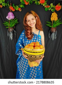 Happy Woman Carrying Fruit Basket Wearing Light Blue Scarf On Black Background With Flowers, Pontianak, West Kalimantan, July 2022