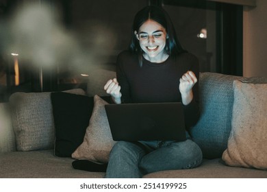 Happy woman celebrates in front of her laptop after achieving a significant success, whether winning a sports bet, acing an exam, landing a new job, or finding a match online. Embracing technology  - Powered by Shutterstock