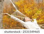 Happy woman celebrating autumn vacation on hammock outstretching arms in a forest