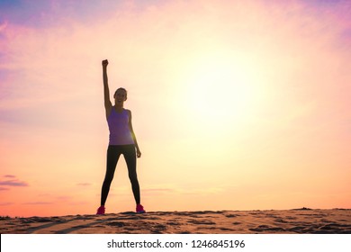 Happy woman celebrating success, silhouette against colorful sky with sunlight.