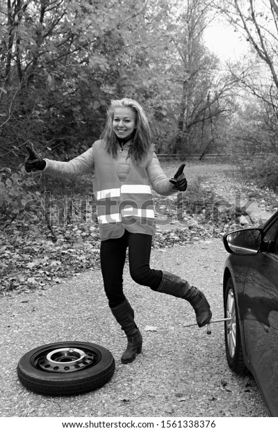 Happy woman changing\
broken wheel on car