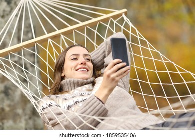 Happy woman checking mobile phone lying on a hammock on holiday in autumn - Powered by Shutterstock