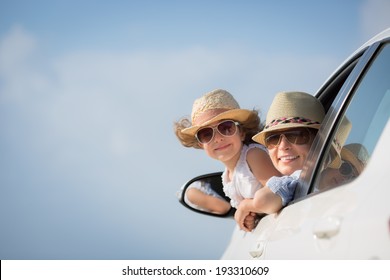 Happy Woman And Child In Car Against Blue Sky Background. Summer Vacation Concept