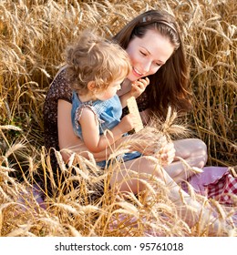 Happy Woman And Child Eating Bread In Spring Wheat Field