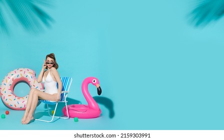 Happy Woman Chilling In Lounge Chair Near Flamingo Rubber Ring On Blue Copy Space Background. Woman Relaxing On Beach In Summer Holiday.