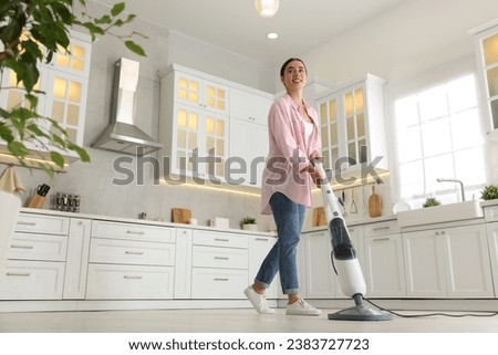 Happy woman cleaning floor with steam mop in kitchen at home, low angle view