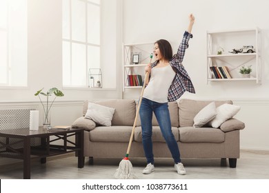 Happy woman cleaning home, singing at mop like at microphone and having fun, copy space. Housework, chores concept - Shutterstock ID 1038773611