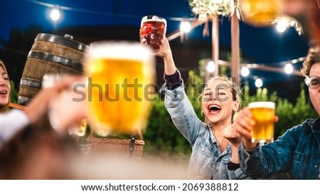 Happy woman clinking and toasting beer at brewery bar restaurant patio with friends - Life style and beverage concept with young people having fun together out side - Focus on face between glasses