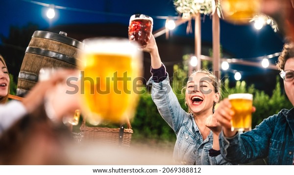Happy woman clinking and toasting beer at brewery
bar restaurant patio with friends - Life style and beverage concept
with young people having fun together out side - Focus on face
between glasses
