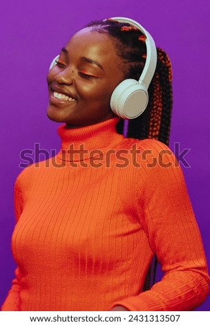 Happy woman with colorful two-tone braids. She stands against a vibrant purple background, wearing casual clothing and headphones. Her modern makeup complement her expression.