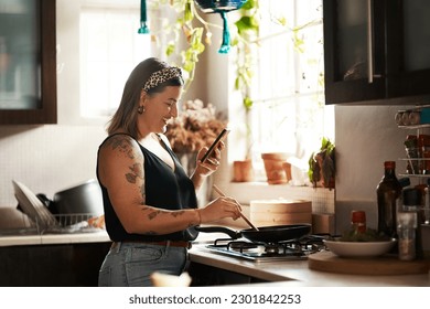 Happy, woman cooking food with smartphone and in kitchen of a home. Dinner or lunch, multitasking and plus size, natural person with tattoo on cellphone following recipe motivation for healthy diet - Powered by Shutterstock