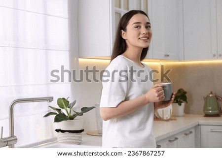 Happy woman with cup of drink in kitchen, space for text. Lazy morning