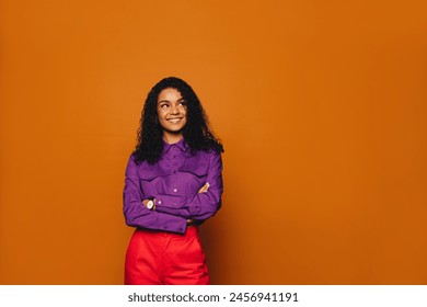 Happy woman with curly hair, in casual clothing, stands in a vibrant studio. Her bright smile reveal her stylish and fashionable personality, as she stands against a orange background - Powered by Shutterstock