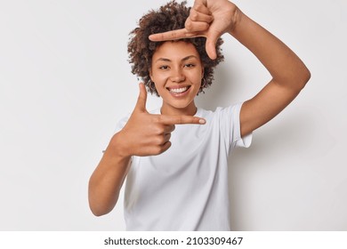 Happy woman with curly hair got inspiration imagines hot to capture interesting shot makes frame gesture smiles gladfully dressed in casual t shirt isolated over white background found great spot - Shutterstock ID 2103309467