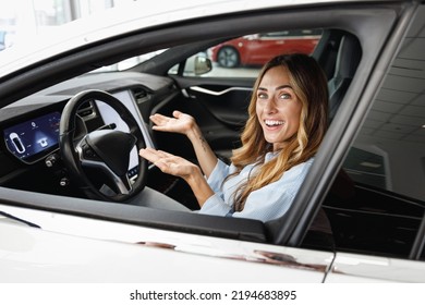 Happy Woman Customer Buyer Client In Blue Shirt Drive Without Holding Steering Wheel Show Autopilot Choose Auto Want Buy New Automobile In Car Showroom Vehicle Salon Dealership Store Motor Show Indoor