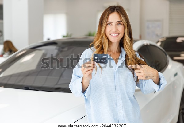 Happy woman customer buyer client in blue shirt\
hold showing credit bank card choose auto want to buy new\
automobile in car showroom vehicle salon dealership store motor\
show indoor. Sales\
concept.