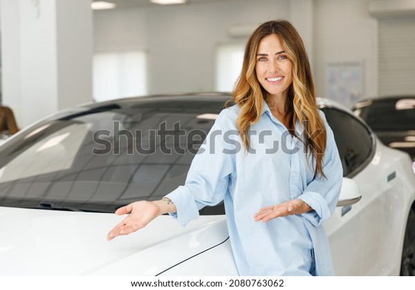 Happy woman customer female buyer client wears\
blue shirt chooses point hands on white auto wants to buy new\
automobile in car showroom vehicle salon dealership store motor\
show indoor. Sales\
concept