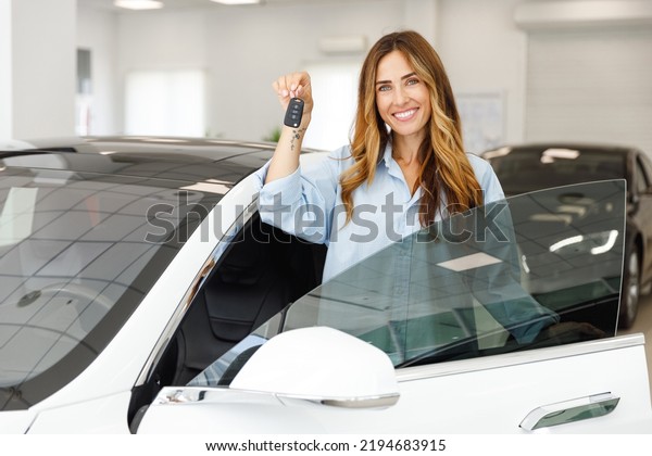 Happy woman customer female buyer client wears\
blue shirt hold keys gets into car chooses auto wants to buy new\
automobile in showroom vehicle salon dealership store motor show\
indoor. Sales concept