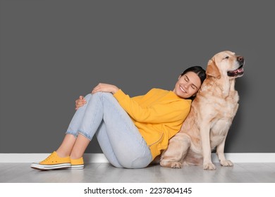 Happy woman with cute Labrador Retriever on floor against grey wall - Powered by Shutterstock