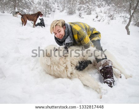 happy woman dabbles with a white dogs in the snow. breed Maremmo Abruzza Sheepdog