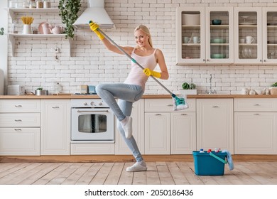 Happy woman dancing with mop and having fun while cleaning home. Active excited housekeeper cleaner housewife doing wet disinfection.