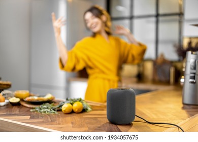 Happy Woman Dancing On The Kitchen During A Breakfast Time, Listening To The Music From A Smart Speaker At Home