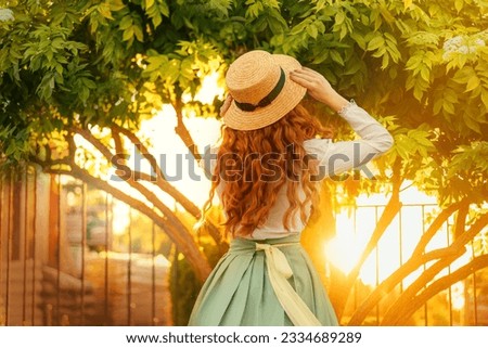 happy woman dancing spinning in vintage straw hat, girl long curly red hair fly wind, retro lady old style white blouse mint skirt dress back rear view. green tree magic sun light flare summer nature