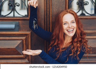 Happy Woman Dangling Keys Over Flat Hand While Standing In Front Of Wooden Door With Wrought Iron Windows