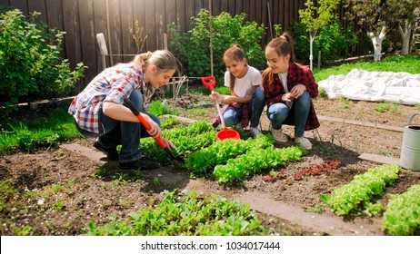 Happy Woman With Daughters Planting Seeds In Garden