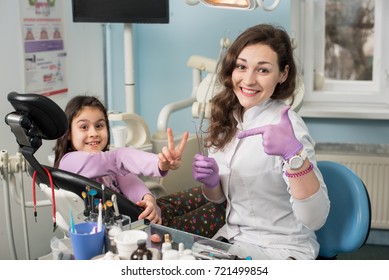 Happy woman dentist and girl patient after treating teeth at dental office, smiling and looking to the camera. Dentistry, medicine, stomatology and health care concept. Dental equipment