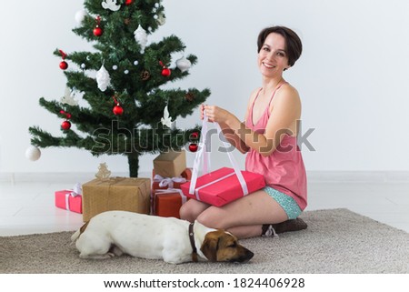 Happy woman with dog opening Christmas gifts. Christmas tree with presents under it. Decorated living room