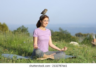Happy woman doing yoga in a meadow distracted with a bird on head