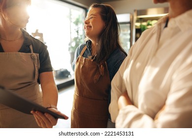 Happy woman with Down syndrome smiling cheerfully while standing in a staff meeting in a grocery store. Group of diverse women working together in an all-female small business. - Powered by Shutterstock