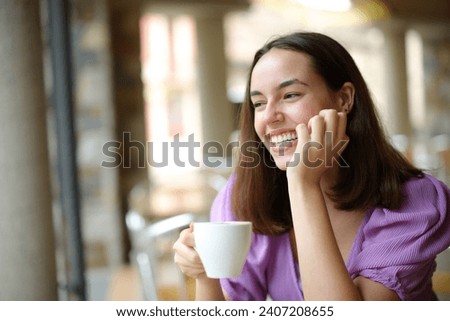 Happy woman drinking coffee contemplating and laughing in a restaurant terrace