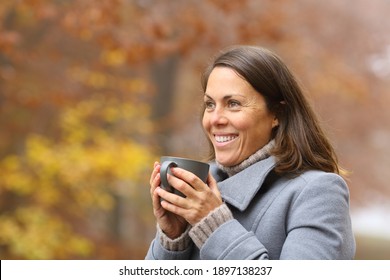 Happy Woman Drinking Coffee Looking Away In Winter Outside In A Park