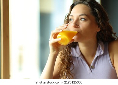 Happy woman drinking orange juice looking through window - Powered by Shutterstock