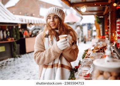 Happy woman drinks a hot drink from a glass and walks through the Christmas market on a sunny winter day. Spending winter holidays. Holiday concept. - Powered by Shutterstock