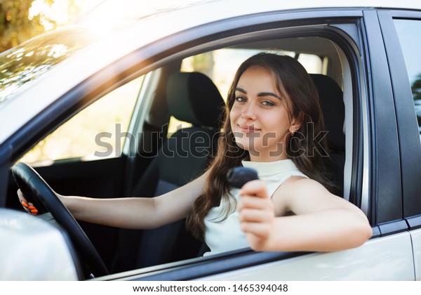 Happy woman driver brag about\
receiving driving license showing car key to the camera feeling\
happy and in high spirit. Young student girl has got her first\
car