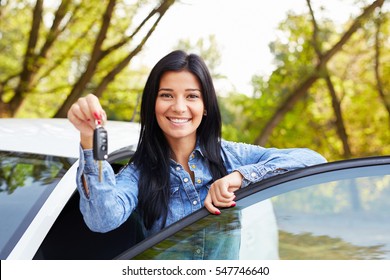 Happy woman driver showing car keys and leaning on car door