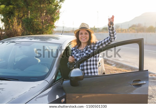Happy woman driver showing car keys and leaning on\
car door