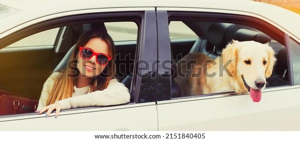 Happy woman driver and young Golden\
Retriever dog sitting in car looking out the\
window