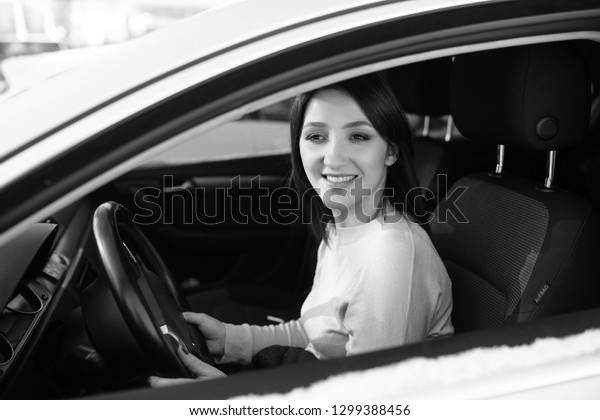 Happy woman driving a car outdoors in winter, black\
and white frame