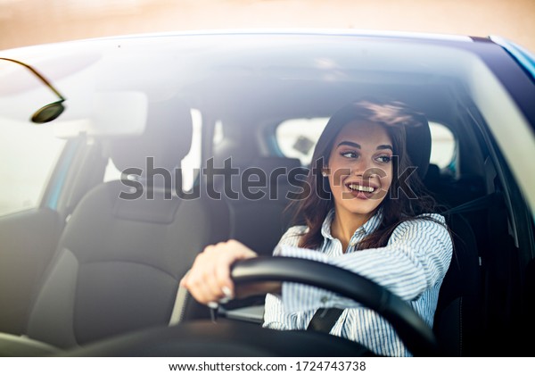 Happy woman driving a car and\
smiling. Cute young success happy brunette woman is driving a car.\
Portrait of happy female driver steering car with safety\
belt