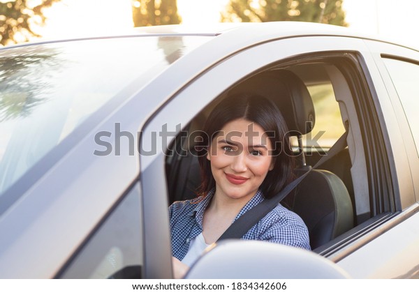 Happy woman driving a car and smiling. Cute\
young success happy woman is driving a car. Portrait of happy\
female driver steering car with safety\
belt